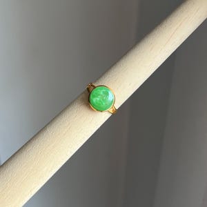 May include: A gold ring with a green oval-shaped stone. The stone has a marbled pattern.