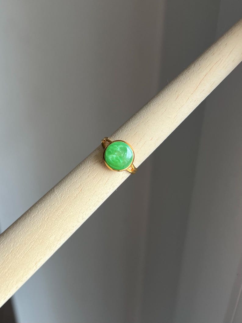 May include: A gold ring with a green oval-shaped stone. The stone has a marbled pattern.
