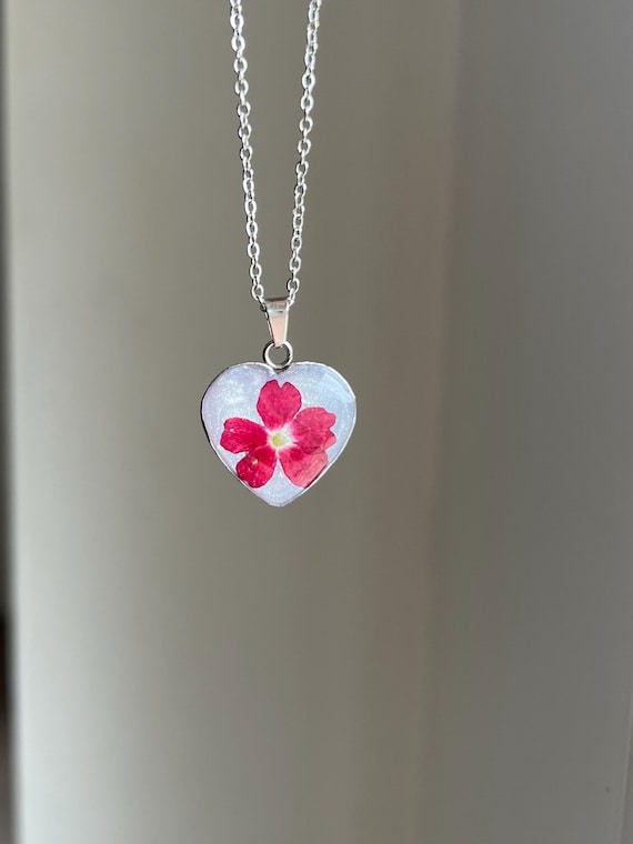 Love pendant heart shape stainless steel in silver light glitter background with a real red flower real flower jewelry