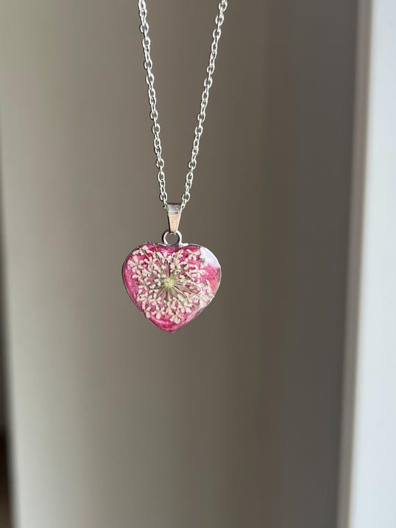 Love pendant heart shape stainless steel in silver pink glitter background with white real flowers real flower jewelry