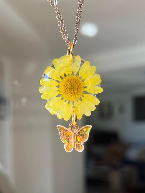 Necklace pendant made of a real yellow daisy flower with golden clasp and butterfly charm glitter