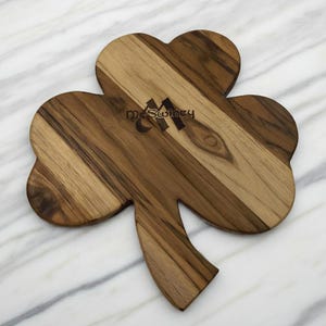 Pu&ograve; includere: Un tagliere in legno a forma di trifoglio caratterizzato da una venatura naturale del legno con varie tonalit&agrave; di marrone. Il tagliere &egrave; inciso con il testo McSwiney in un carattere scuro e stilizzato nella parte superiore del trifoglio.