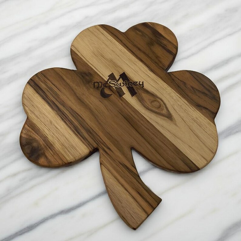 Pu&ograve; includere: Un tagliere in legno a forma di trifoglio caratterizzato da una venatura naturale del legno con varie tonalit&agrave; di marrone. Il tagliere &egrave; inciso con il testo McSwiney in un carattere scuro e stilizzato nella parte superiore del trifoglio.