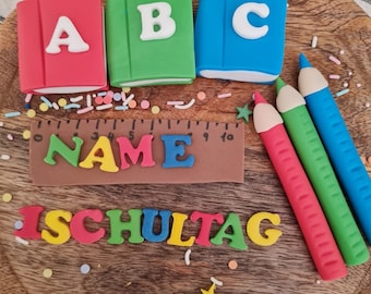 May include: A wooden cake board decorated with colorful sprinkles, fondant letters spelling "NAME" and "ISCHULTAG", three fondant pencils, and three fondant books with the letters "A", "B", and "C" on them.