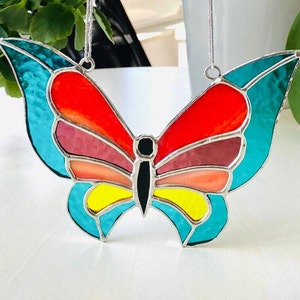May include: A stained glass butterfly with teal, red, pink, orange, and yellow wings. The butterfly is hanging from a silver chain.