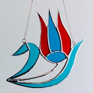 May include: A stained glass suncatcher with a blue and red abstract design. The suncatcher is hanging from a silver chain.
