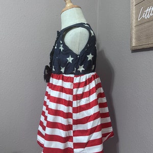May include: A sleeveless dress for a child, featuring a blue and white American flag print on the top and red and white stripes on the bottom.