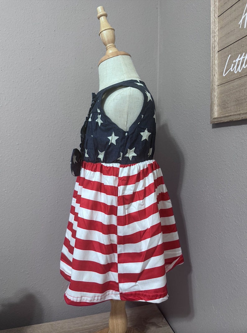 May include: A sleeveless dress for a child, featuring a blue and white American flag print on the top and red and white stripes on the bottom.