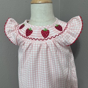 K&ouml;nnte beinhalten: Rosa-wei&szlig;es Gingham-Babykleid mit gestickten Erdbeeren am Ausschnitt.