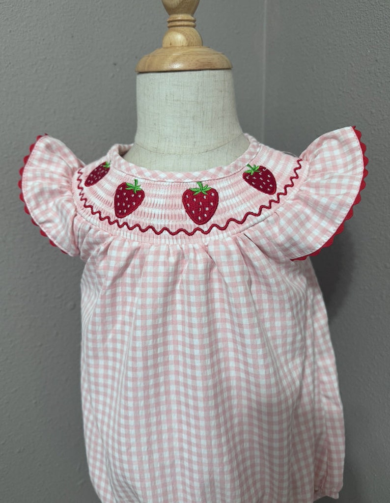 K&ouml;nnte beinhalten: Rosa-wei&szlig;es Gingham-Babykleid mit gestickten Erdbeeren am Ausschnitt.