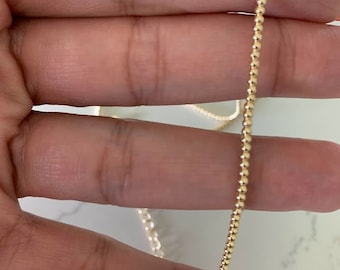 May include: A gold beaded chain necklace. The chain is made of small, round beads that are evenly spaced.