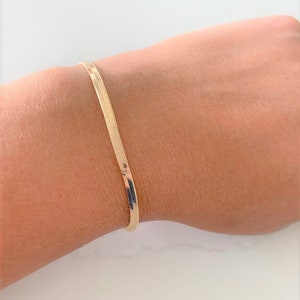 May include: A gold-toned snake chain bracelet on a person's wrist.