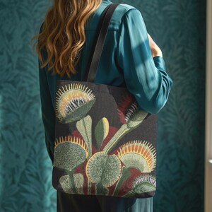 May include: A black tote bag featuring a detailed woven design of multiple Venus flytrap plants. The botanical illustration displays green, yellow, and red hues on the leaves and traps. The bag includes two black shoulder straps for carrying.