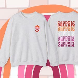 May include: A grey sweatshirt with a pink and orange flower on the front and the word "Sapphic" repeated five times in a rainbow pattern on the back.