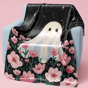 May include: A soft throw blanket featuring a black background with a white ghost character and numerous pink flowers. The upper portion displays a starry night sky pattern, while the lower section is filled with various pink blossoms on green stems.