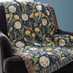 May include: A woven throw blanket featuring a dark navy blue background with a repeating pattern of yellow dandelion flowers, white dandelion seed heads, and green stems. The blanket has a textured finish and decorative fringe along the edges.