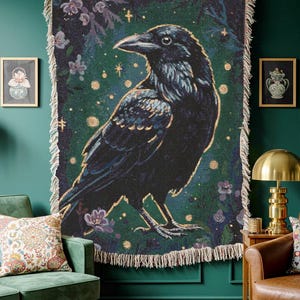 Raven woven blanket with a side profile of a raven with a yellow highlight around it a teal background and flowers in the corners witchy tapestry