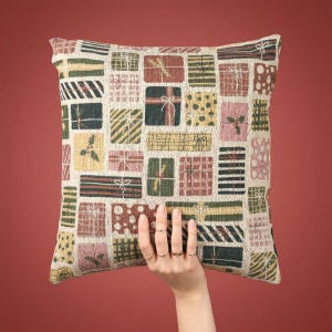 Könnte beinhalten: Ein quadratisches Zierkissen mit einem gewebten Gobelinmuster aus verschiedenen rechteckigen Geschenkboxen in Grün-, Rot-, Rosa- und Gelbtönen. Das Design umfasst diverse Motive wie Streifen, Punkte und Stechpalmenblätter mit Schleifen.