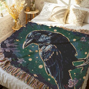 Raven woven blanket with a side profile of a raven with a yellow highlight around it a teal background and flowers in the corners witchy tapestry