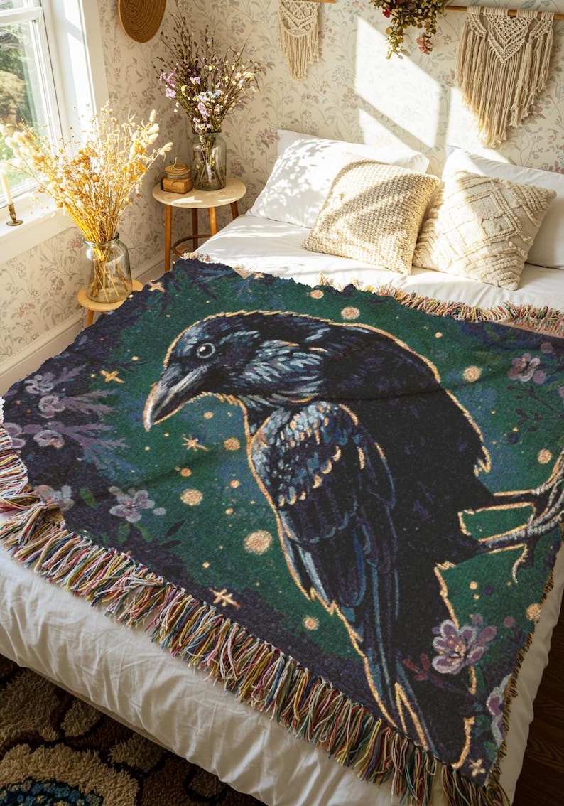 Raven woven blanket with a side profile of a raven with a yellow highlight around it a teal background and flowers in the corners witchy tapestry