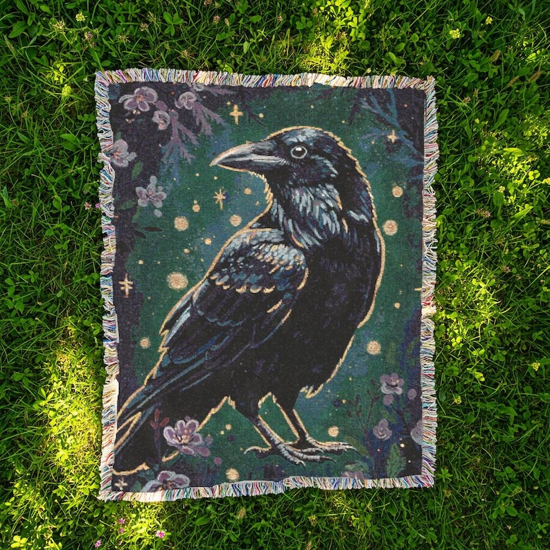 Raven woven blanket with a side profile of a raven with a yellow highlight around it a teal background and flowers in the corners witchy tapestry