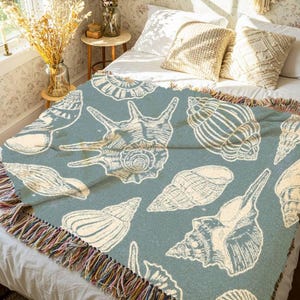 May include: A blue throw blanket with a white seashell pattern. The blanket has a fringe border with multicoloured threads.