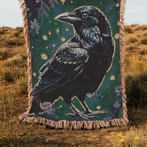 Raven woven blanket with a side profile of a raven with a yellow highlight around it a teal background and flowers in the corners witchy tapestry