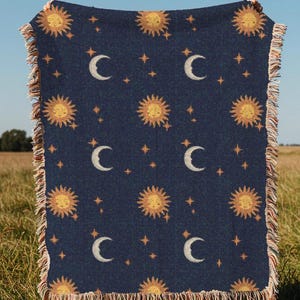 Peut inclure: Une couverture tissée avec un fond bleu marine et un motif répété de soleils jaunes, de croissants de lune blancs et de petites étoiles blanches.