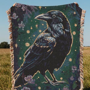 Raven woven blanket with a side profile of a raven with a yellow highlight around it a teal background and flowers in the corners witchy tapestry
