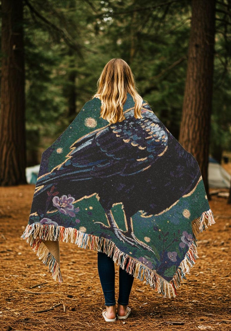 Raven woven blanket with a side profile of a raven with a yellow highlight around it a teal background and flowers in the corners witchy tapestry