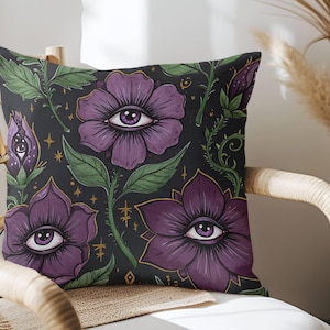Puede incluir: Almohada floral de color morado y verde con un estampado integral de flores estilizadas con ojos. El fondo es negro.