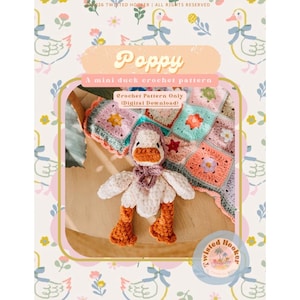 May include: A crochet pattern for a mini duck named Poppy. The duck is white with an orange beak and feet, wearing a purple scarf and hat. The background features a colorful, crocheted blanket with floral patterns.