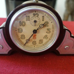 May include: A vintage black and silver alarm clock with a white face and black hands. The clock has a decorative design on the sides and the words "Made in France" are printed on the face.