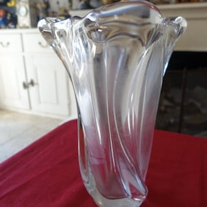 May include: A clear glass vase with a wavy, organic design. The vase is tall and slender, with a wide opening at the top.