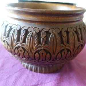 May include: A dark brown wooden bowl with intricate carved floral designs. The bowl has a wide rim and a rounded base.