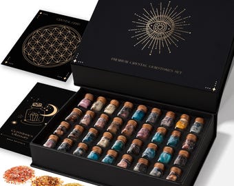 May include: A black box set with a gold design and the text "Premium Crystal Gemstones Set" contains small glass bottles filled with colorful gemstones. Two black cards with gold designs are next to the box. Several piles of gemstones are in the foreground.