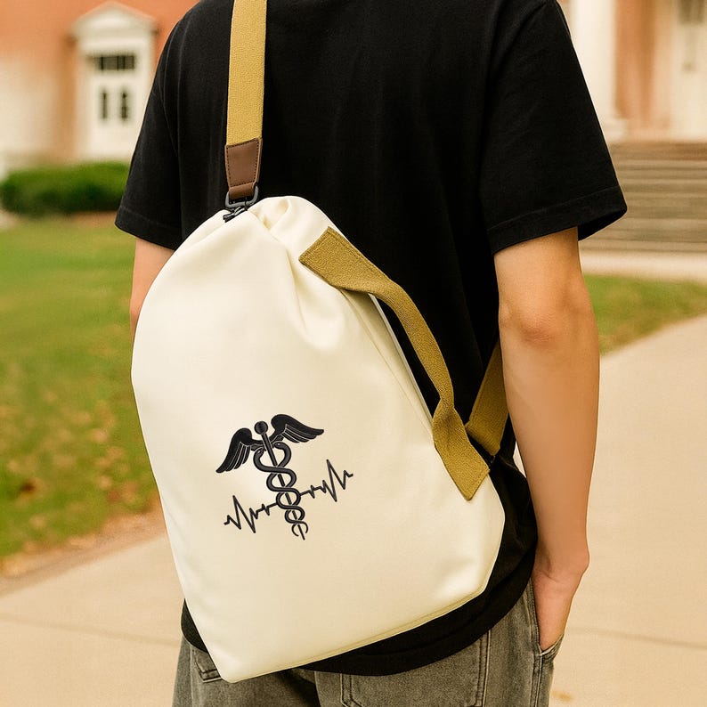 May include: Cream-coloured drawstring backpack featuring a black medical symbol and heartbeat line design. The bag has olive green straps and a brown leather accent. The bag is worn over the shoulder.