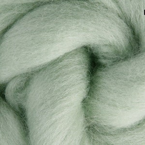 May include: Close-up of mint-coloured wool roving. The soft, fluffy fibres are tightly packed, creating a dense texture. The word "Mint" is printed in a black font in the upper right corner. This wool is ideal for various fibre art projects.