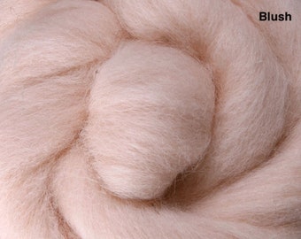 May include: Close-up of a pile of blush-colored wool roving. The soft, fluffy fibers are tightly packed together, creating a dense texture. The word "Blush" is printed in black in the upper right corner. This wool is suitable for various fiber art projects.