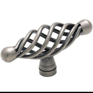 May include: A decorative cabinet pull with a cage-like design. The metal pull has a twisted, cage-like design with a ball-shaped end on each side. The pull is a muted gray color and is mounted on a small, round base.