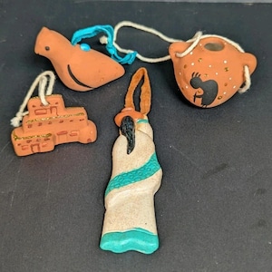 May include: Four terracotta ornaments with string hangers. The ornaments include a bird, a building, a pot with a Kokopelli figure, and a figure in a robe with a hat.