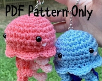 May include: Two crocheted jellyfish keychains, one pink and one blue, with black eyes and smiling mouths. The keychains are hanging from a silver chain.