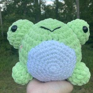May include: A green crocheted frog plush toy with white crocheted belly and black eyes.