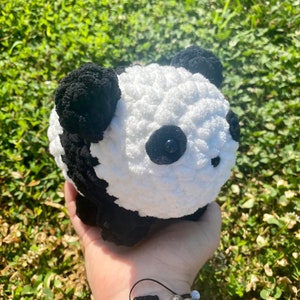 May include: A crocheted panda plush toy with black and white fur. The panda has black eyes and a black nose.
