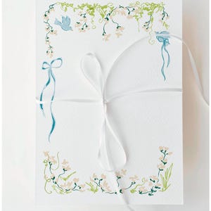 Könnte beinhalten: Weiße Karte mit floralen und Vogelillustrationen in Grün, Hellrosa und Türkis. Ein weißes Band ist um die Karte gebunden. Das florale Design umfasst kleine Blüten und Ranken, mit einem türkisfarbenen Vogel.