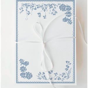 Può includere: Un biglietto bianco con un motivo floreale blu e bordi smerlati. Il biglietto è legato con un nastro bianco. Il motivo floreale comprende viti e grappoli di fiori, creando un'estetica elegante.