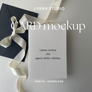 Puede incluir: Una maqueta de tarjeta blanca con una cinta blanca atada alrededor de un sobre negro. La tarjeta está en blanco y tiene el texto "1 photo mockup JPG approx 4000 x 3000px" y "DIGITAL DOWNLOAD" impreso en ella. El texto "LYRAH STUDIO CARD mockup" está impreso encima de la tarjeta.