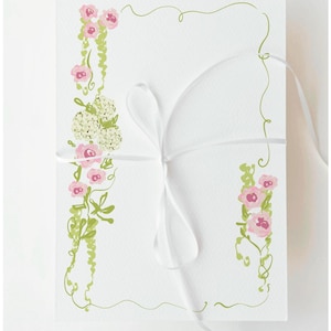 Könnte beinhalten: Weiße Karte mit weißem Band gebunden, verziert mit rosa Rosen und grünen Ranken. Das florale Design ist auf die Karte gemalt, mit einem grünen Rand. Die Gesamtästhetik ist zart und elegant, geeignet für Einladungen oder Schreibwaren.