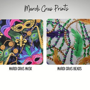 May include: Two fabric prints featuring Mardi Gras themes. The first print is black with purple, green, gold, and pink accents. It features Mardi Gras masks, feathers, fleur-de-lis, and beads. The second print is white with gold, green, and purple accents. It features Mardi Gras beads and feathers.