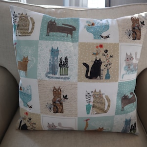 Pu&ograve; includere: Un cuscino decorativo con un design a patchwork che presenta diverse illustrazioni di gatti in varie pose e colori. Lo sfondo &egrave; una miscela di blu chiaro, beige e bianco.